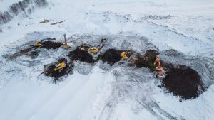 Mini ekskavatorius dirba žiemos sąlygomis statybų aikštelėje.